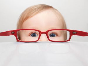 toddle boy with red glasses peering over table