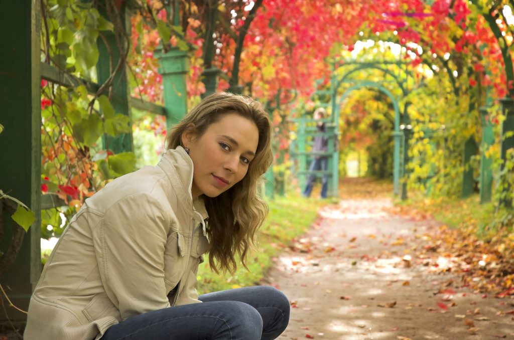 College-age girl sitting outside in the autumn leaves.