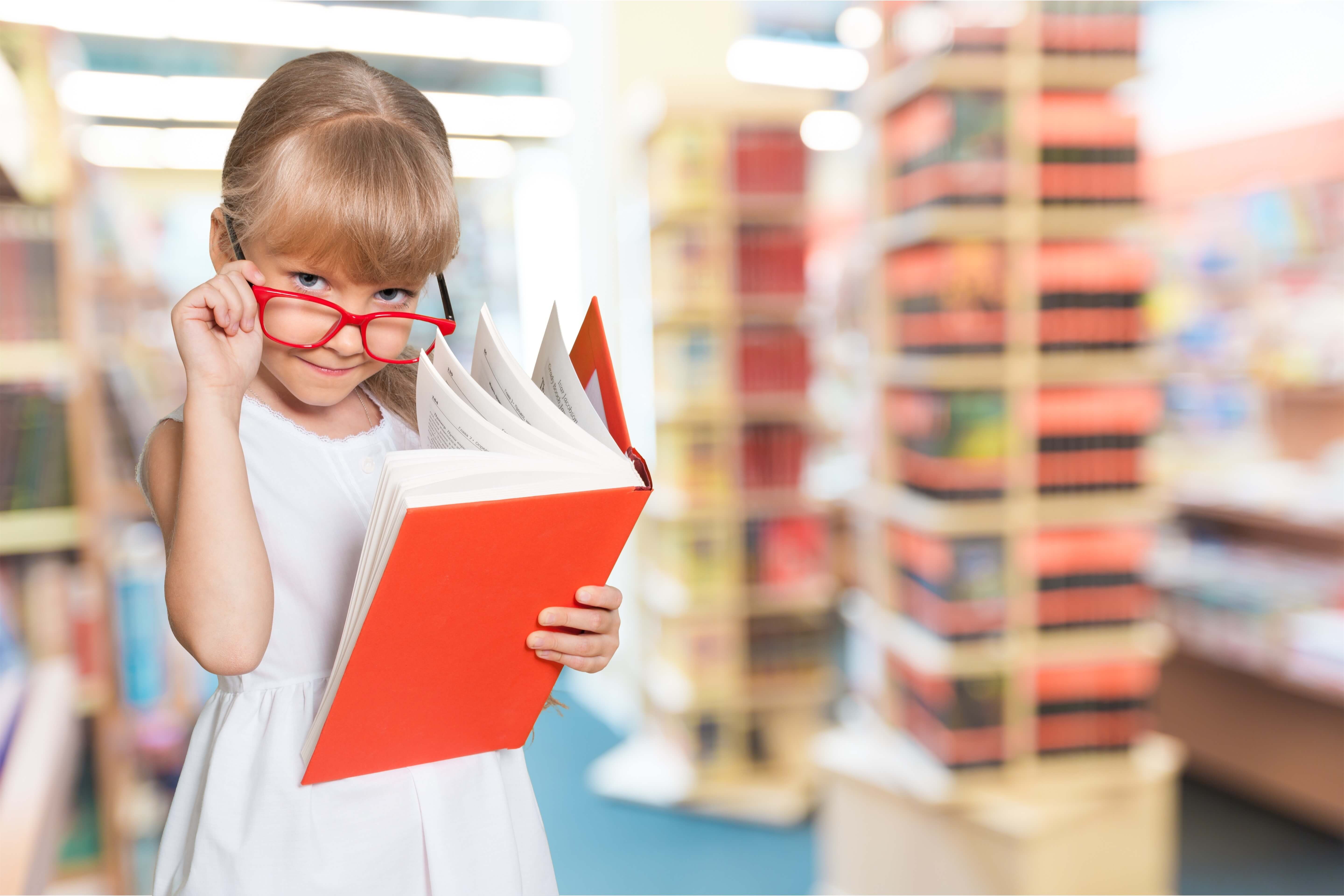 Little girl with glasses reading a book in the library