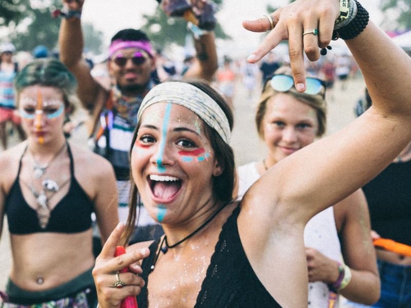 Woman with painted face dancing at a concert and smiling.