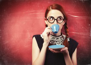 Woman with glasses sipping coffee and looking to the side.
