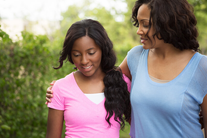 Mother with her arm around teen daughter while having an honest conversation about consent