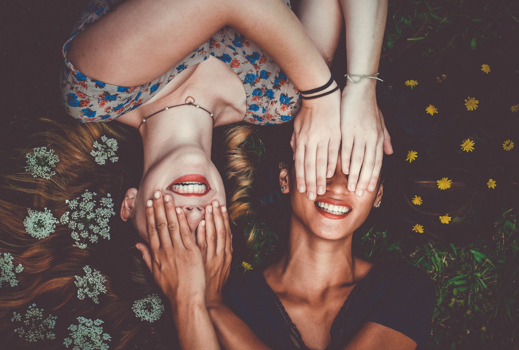 Two women lying on the ground covering each other's eyes.