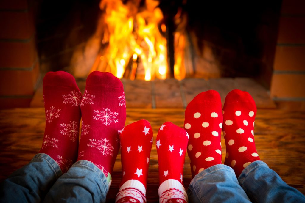 Three pairs of feet with Christmas socks in front of a cozy fire. They put their smartphones away